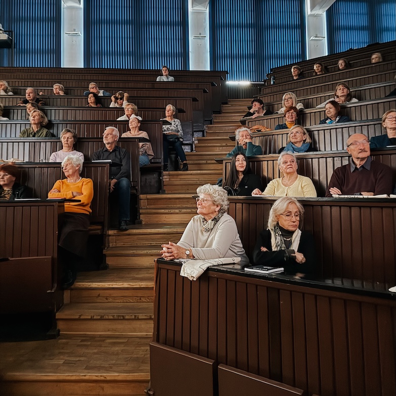 Akademia Seniora Duża grupa seniorów znajduje się w auli akademickiej i słucha wykładu w ramach „Akademii Seniora