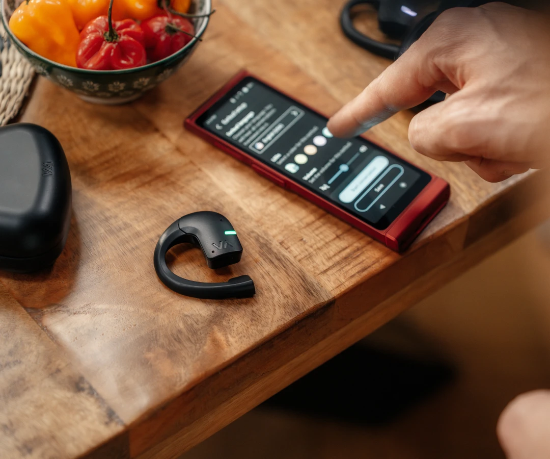 a hand selecting options on a hand-held translator with a translating earbud lying next to it