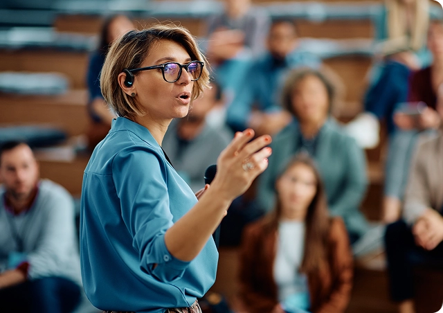 A woman giving a speech at a university, wearing a Vasco Translator E1 in her ear.