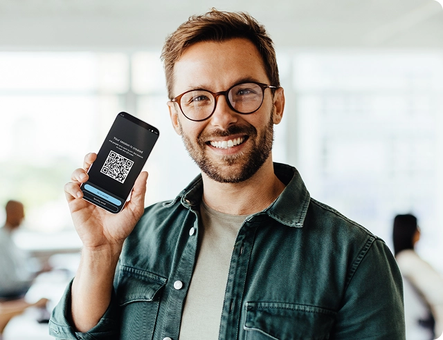 A smiling man holding a smartphone displaying a QR code for joining Vasco Audience.