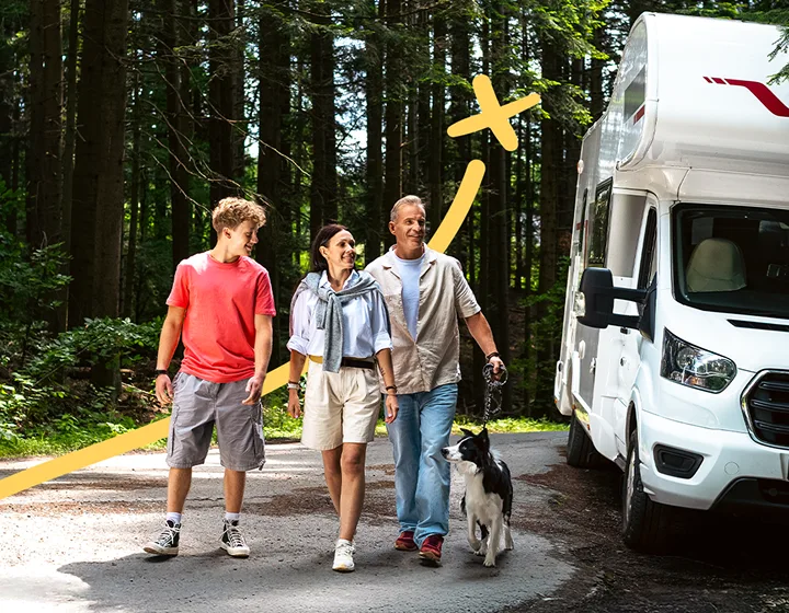 Trzyosobowa rodzina – dwoje rodziców i jedno dziecko – wraz z psem, oddalająca się od zaparkowanego kampera w słoneczny dzień. Uśmiechają się, rozmawiają i cieszą się swoim towarzystwem.