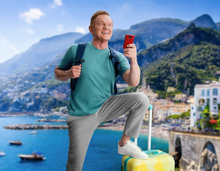 Cezary Pazura stojący za prezentami, w zimowym swetrze, trzyma w rękach pudełko z Vasco Translatorem.