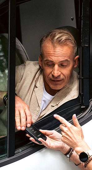 Mężczyzna siedzący w samochodzie mówi do urządzenia Vasco Translator Q1, które ktoś mu podaje.