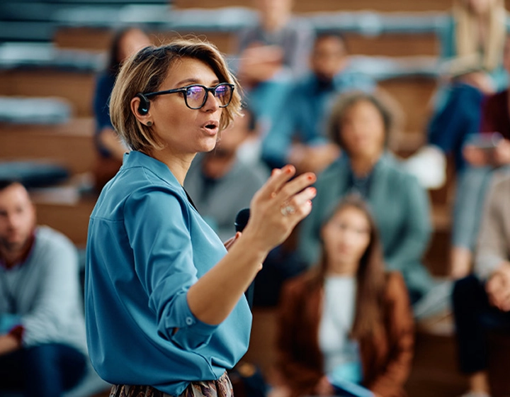 Kobieta wygłaszająca przemówienie na uniwersytecie, mająca w uchu urządzenie Vasco Translator E1.