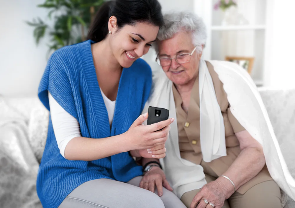 Kobieta pokazuje starszej kobiecie urządzenie Vasco Translator Q1, demonstrując jego przydatność w pomaganiu osobom starszym.